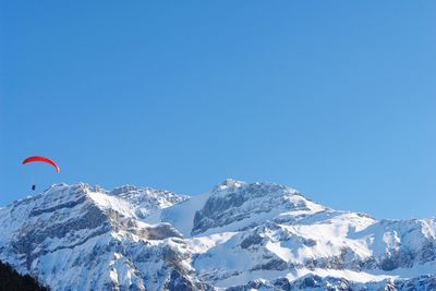 Person paragliding over snowcapped mountains against clear blue sky