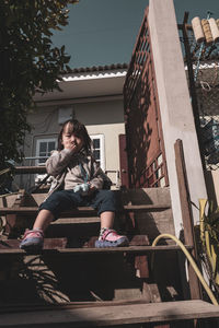 Low angle portrait of girl sitting on staircase during sunny day