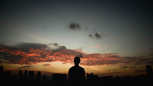 Silhouette of man overlooking city during sunset