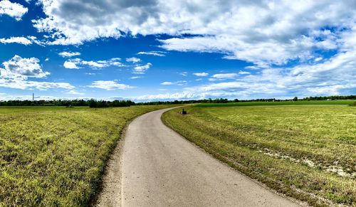 Empty road amidst field against sky
