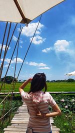 Rear view of woman standing by plants against sky