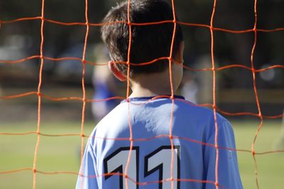 Rear view of boy seen though chainlink fence