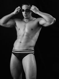 Man wearing swimming goggles while standing against black background