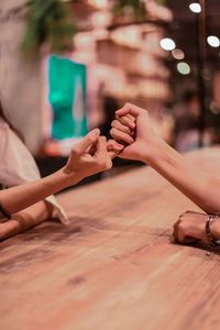 Cropped hands of female friends doing pinky promise at table in restaurant