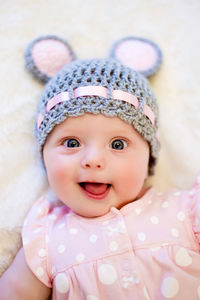 Baby girl lying on her back and smiling on the bed in pink clothes and hat with ears