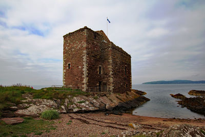 Old building by sea against sky