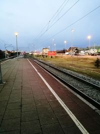 Railroad tracks in illuminated station against sky