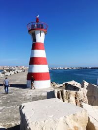 Lighthouse on beach against clear blue sky