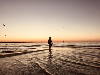 Silhouette woman standing at beach against sky during sunset