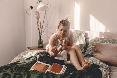 Young woman sitting on bed at home