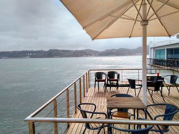 Empty chairs and tables at restaurant by sea against sky