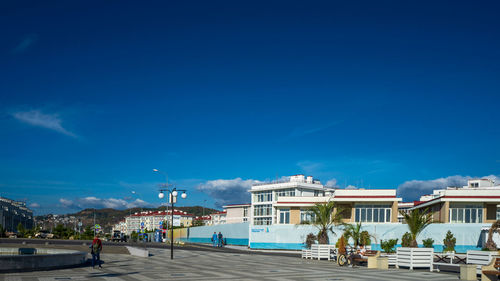 People on street by buildings against blue sky