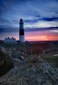 Lighthouse by sea against sky during sunset