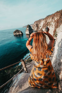 Rear view of woman on rock by sea against sky