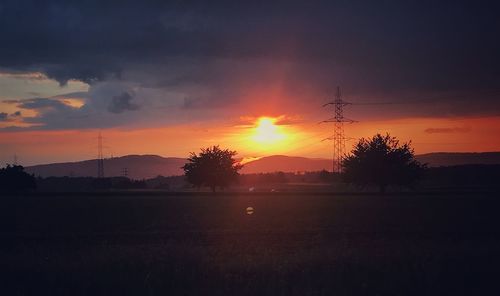 Silhouette trees on field against sky during sunset