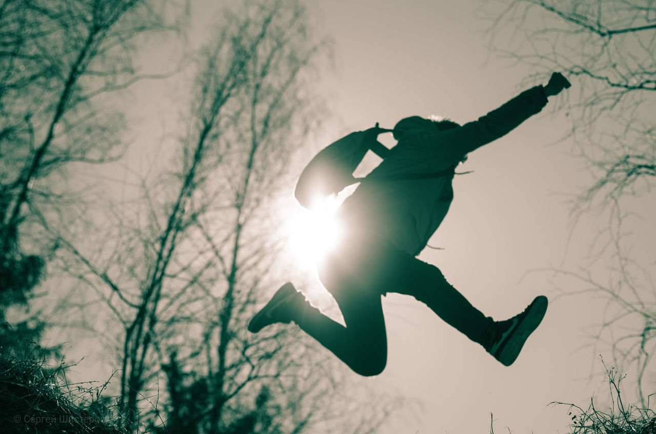 LOW ANGLE VIEW OF MAN JUMPING AGAINST TREE