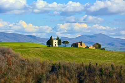 Farmhouses in field against cloudy sky