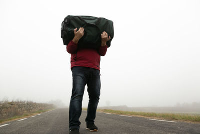 Carrying a suitcase in his arms an unrecognizable man walking along a road on a foggy day