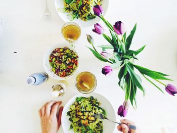 Cropped hands having salad by purple tulips on table