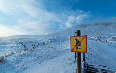 Road sign on snow covered landscape against sky