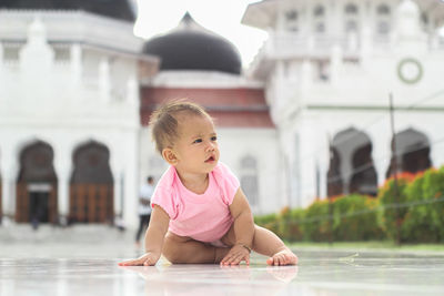 A cute baby girl sits in front of the baiturrahman grand mosque, banda aceh, indonesia