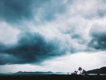 Silhouette of trees on landscape against cloudy sky