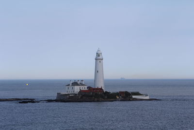 Lighthouse by sea against clear sky