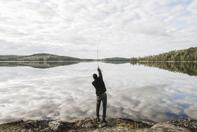 Rear view of man fishing in lake during vacation