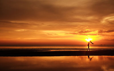 Silhouette woman standing on beach against orange sky