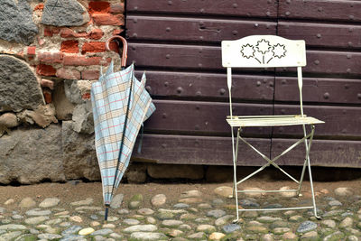 Chair and umbrella on sidewalk against wall