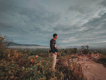 Side view of young man standing on land against sky