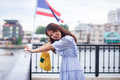 Portrait of woman standing by railing against flag and buildings in city