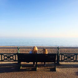 Rear view of mother and daughter looking at sea view against clear blue sky