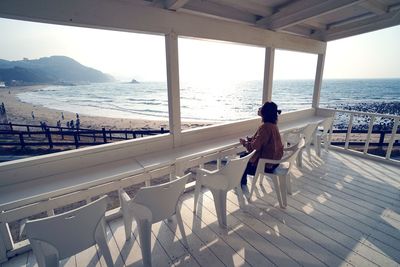 Side view of woman sitting on chair at observation point by sea