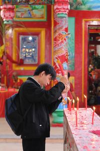 Side view of man igniting incense stick at temple