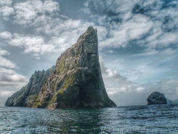 View of cliff in ocean against cloudy sky