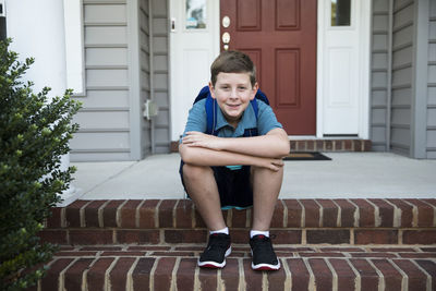 Tween boy with backpack sits on front house steps, first day of school