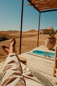Low section of woman relaxing on beach against clear sky