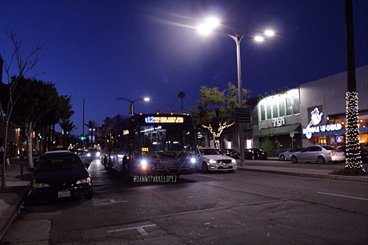 street light, illuminated, night, transportation, car, land vehicle, street, mode of transport, lighting equipment, building exterior, road, city, sky, city street, tree, built structure, traffic, architecture, city life, outdoors