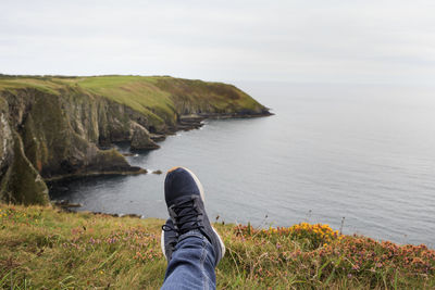 Low section of man on cliff by sea against sky