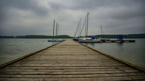 Sailboat on pier at sea against cloudy sky