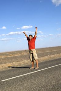 Full length of man with arms raised standing on road against sky