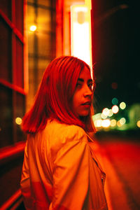 Portrait of woman standing by illuminated street at night