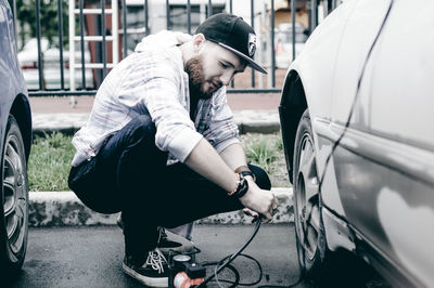 Young man inflating car tire with air pump at parking lot