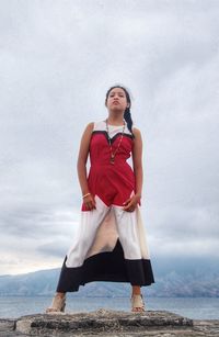 Young woman standing at beach against cloudy sky