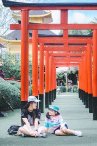 Full length of woman sitting with daughter by torii gate