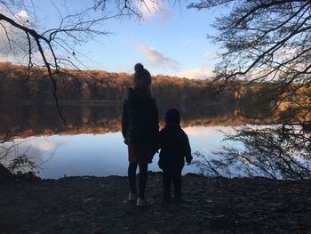 Rear view of siblings standing at lake against sky