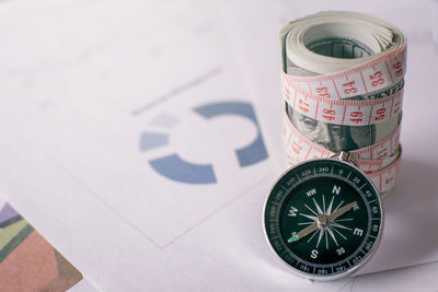 Close-up of navigational compass and paper currencies tied with tape measure on paper