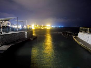 Illuminated bridge over river against sky at night