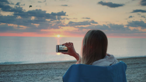 Rear view of woman photographing sea during sunset